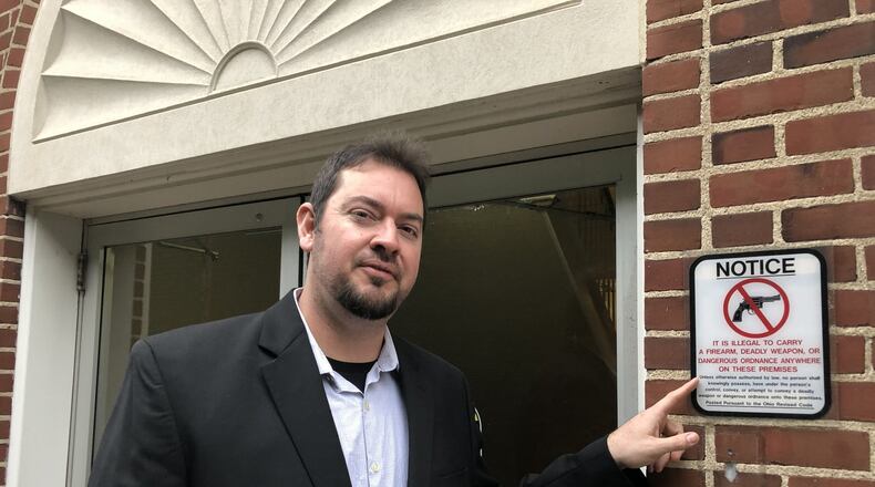 Lebanon City Councilman Joe Shafer points at one of the signs prohibiting the carrying of a firearm into city hall. Shafer and other council members have directed the law director to draft legislation to permit them to conceal-carry during meetings. STAFF/LAWRENCE BUDD