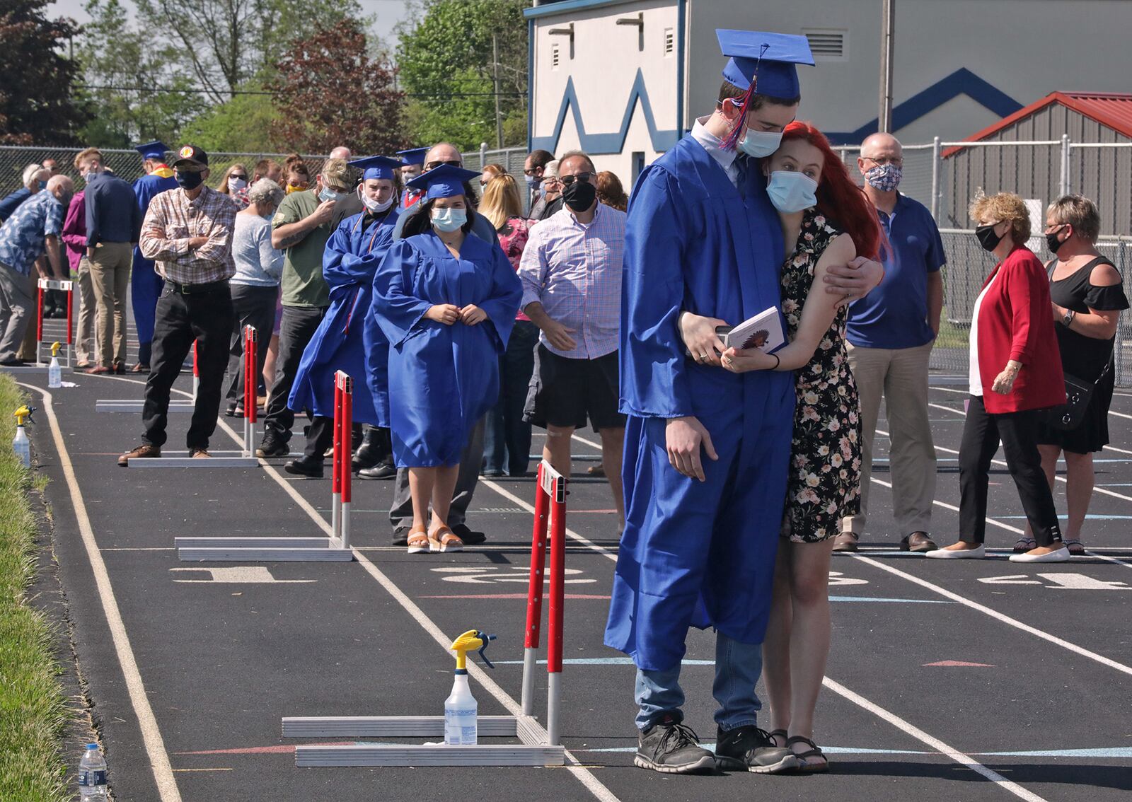 Northwestern senior Michael Akers gets a hug from his girlfriend, Hayley Clark, as he waits with his family to graduate outside at Taylor Field. Students were allowed to bring up to 10 guests and they were staged around the running track in alphabetical order while they waited to receive the diploma. BILL LACKEY/STAFF