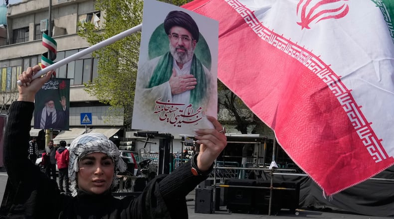 A woman displays a poster of the Iranian Supreme Leader Ayatollah Mojtaba Khamenei as she waves her country's flag during a campaign in support of the government at the Enqelab-e-Eslami, or Islamic Revolution, square in downtown Tehran, Iran, Saturday, March 14, 2026. (AP Photo/Vahid Salemi)