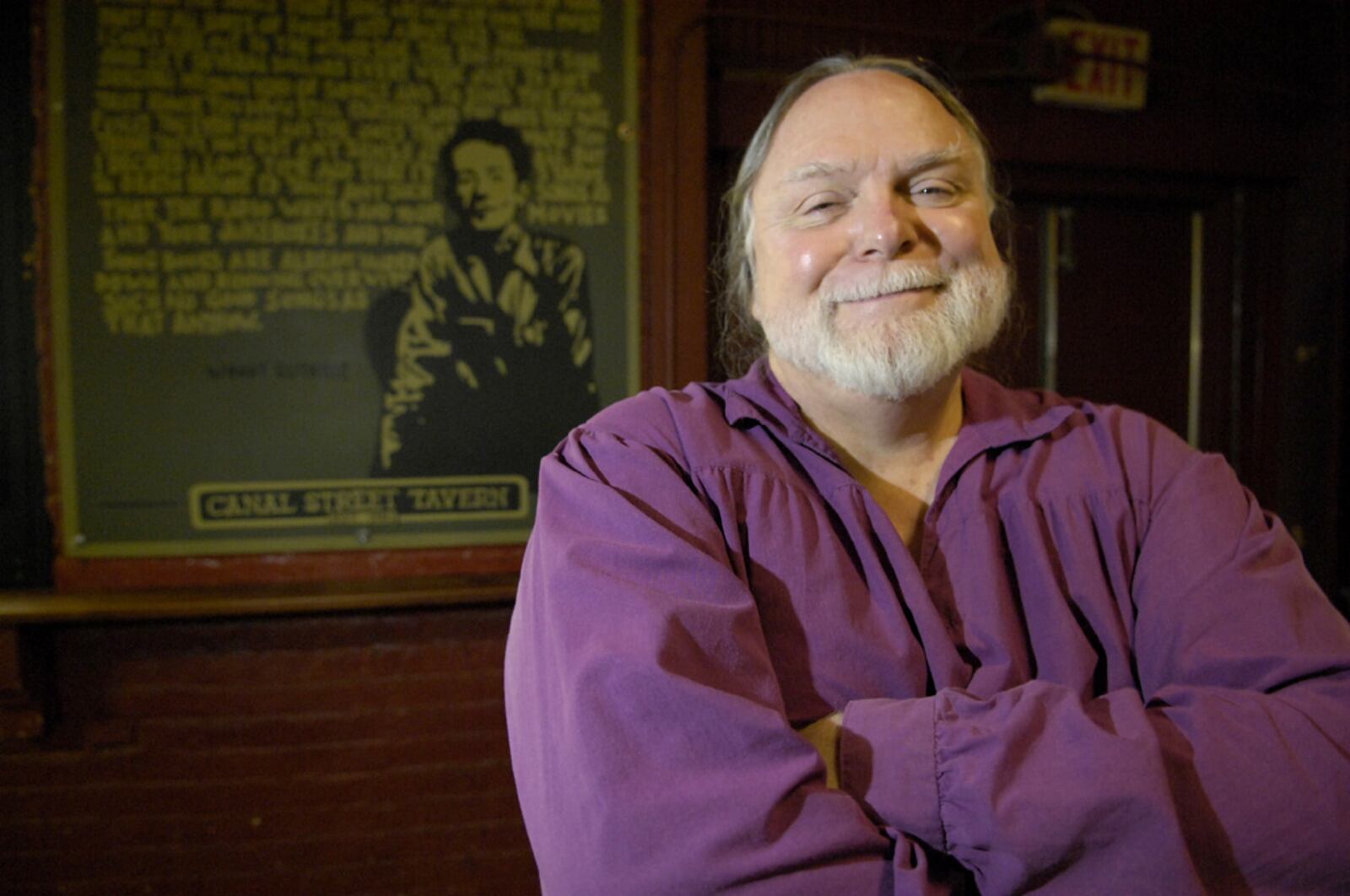 Mick Montgomery, owner of the Canal Street Tavern, poses with the poster of Woodie Guthrie that hangs in the Tavern. The Canal Street Tavern has been a local music venue in Dayton for many years.