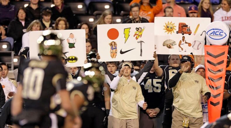 FILE - In this Nov. 6, 2014, file photo, Wake Forest coaches use signs to signal in a play during the first half of an NCAA college football game against Clemson in Winston-Salem, N.C. Once a technique used to replace hand signals for offenses, in the past few years, defenses have started using them, too. (AP Photo/Chuck Burton, File)