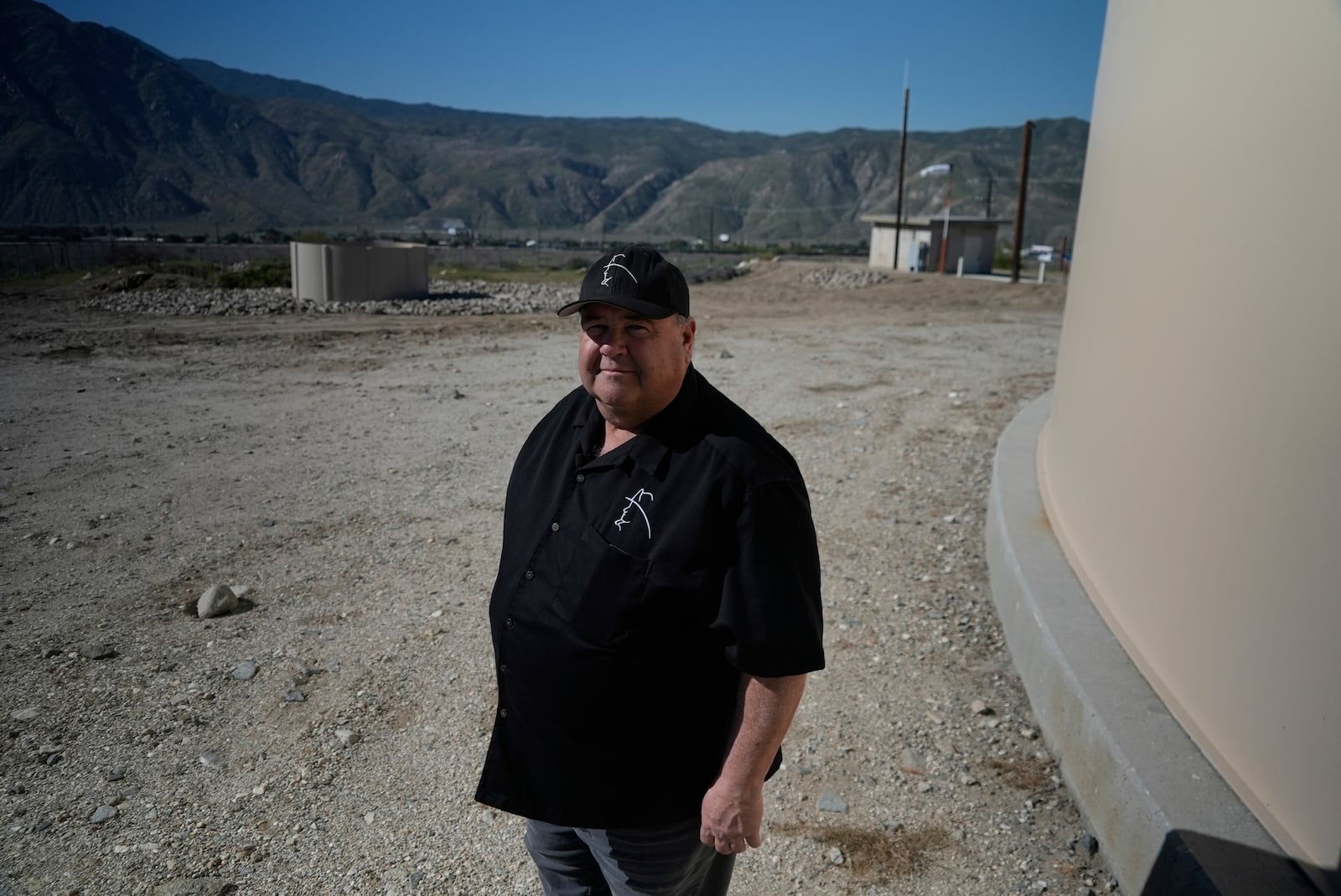 Mark Whaling, a retired firefighter, stands in front of a Heli-Hydrant, a small, open tank that helicopters can rely on to get water faster for urban fires, Friday, April 11, 2025, in Cabazon, Calif. (AP Photo/Brittany Peterson)