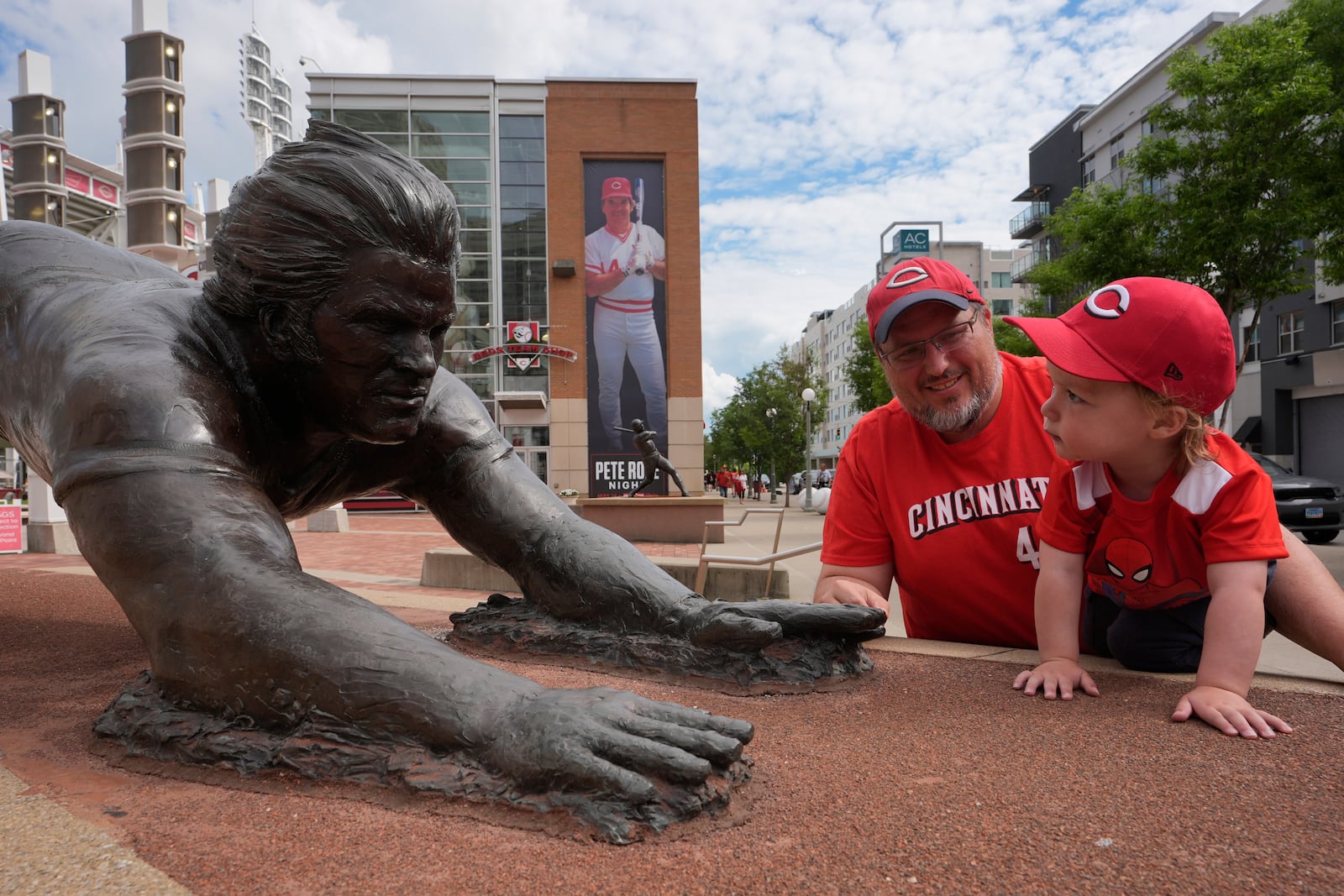 Andrew Scheidt and his one-year-old son Matthew Scheidt visit the bronze statue of former Cincinnati Reds player Pete Rose outside the Great American Ball Park, Tuesday, May 13, 2025, in Cincinnati, before a baseball game between the Cincinnati Reds and the Chicago White Sox, Matthew's first game. (AP Photo/Carolyn Kaster)