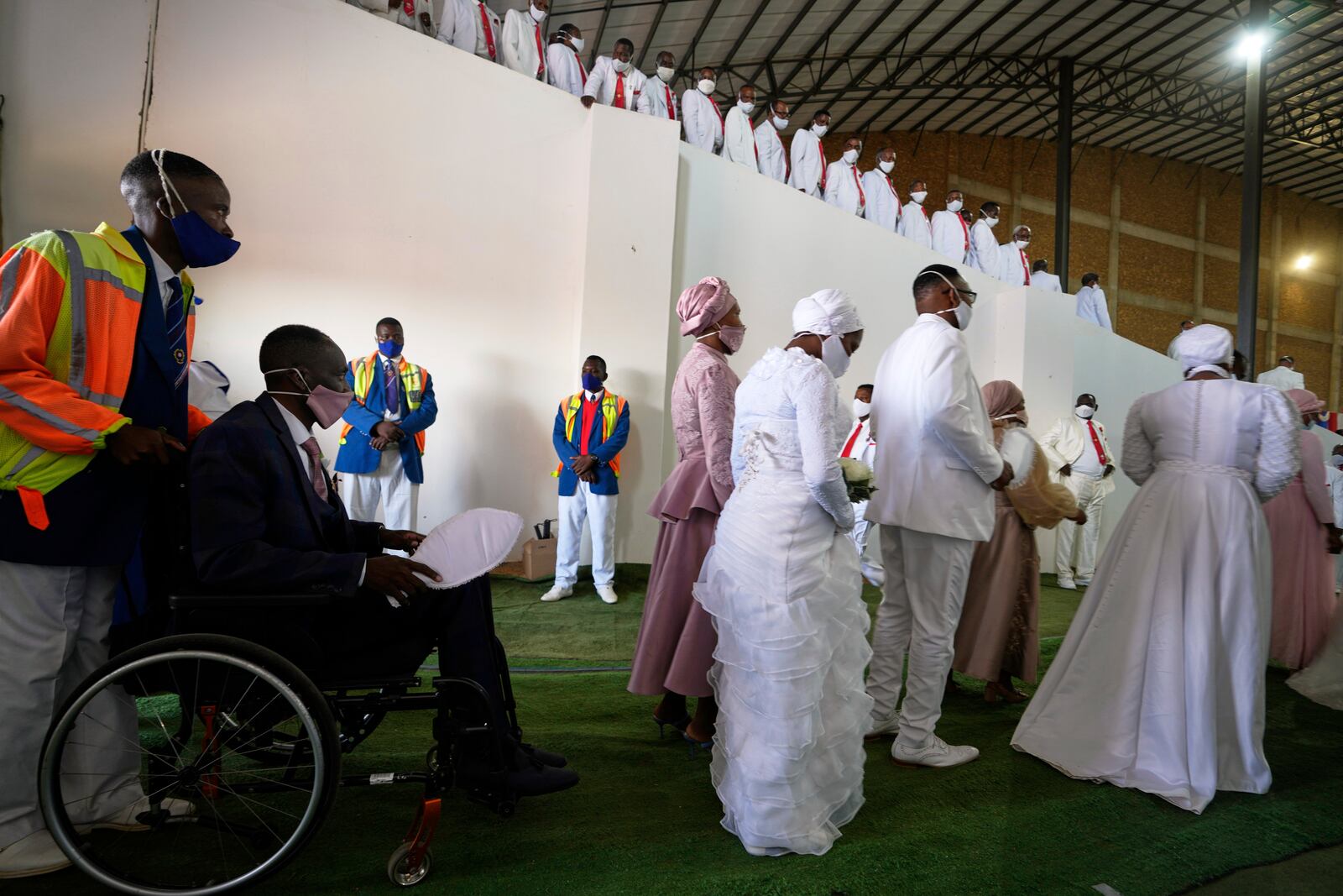 A groom in a wheelchair is assisted by a fellow member whilst his two brides walk in front, during a mass Easter weddings for 3,000 people, some polygamous, at The International Pentecost Holiness Church in Heidelberg, east of Johannesburg, South Africa, Sunday, April 20, 2025. (AP Photo/Themba Hadebe)