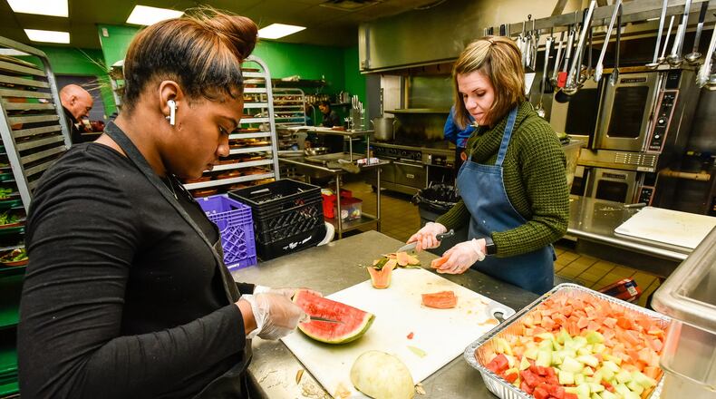 Volunteers Kris’Shawn Fleming, left, and Lisa Henderson cut fruit at House of Bread non-profit community kitchen Friday, Dec. 20, 2019 in Dayton. Fleming is volunteering while she is home from college for the holiday break. NICK GRAHAM/STAFF