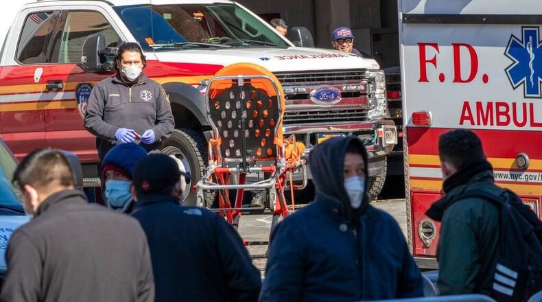 An Emergency Medical Technician works as people line up outside Elmhurst Hospital Center to be tested for the coronavirus, Tuesday, March 24, 2020, in the Queens borough of New York. New York Gov. Andrew Cuomo said the number of positive coronavirus cases in the state surged to more than 20,000, with more than half the cases in New York City.