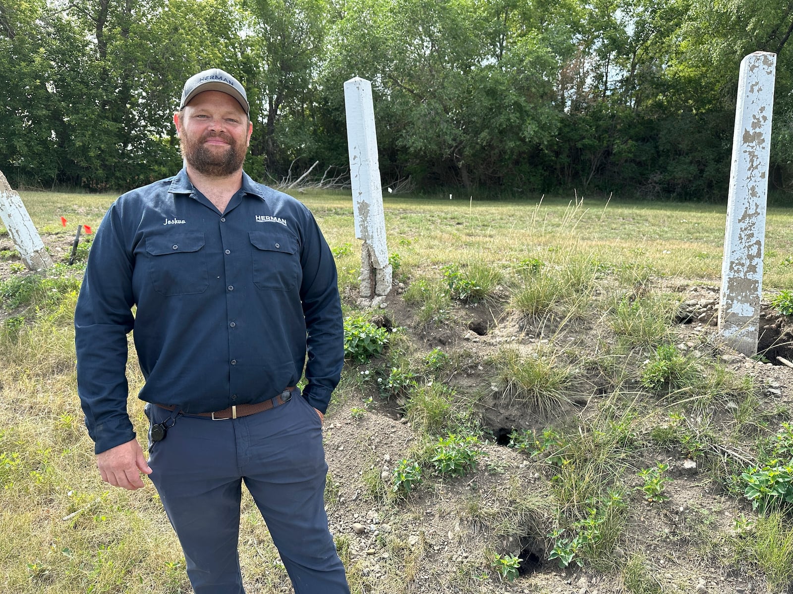 Joshua Herman, owner/operator of Herman Pest Control Services, poses for a photo on Monday, July 14, 2025, next to holes dug by Richardson's ground squirrels in Minot, N.D. (AP Photo/Jack Dura)