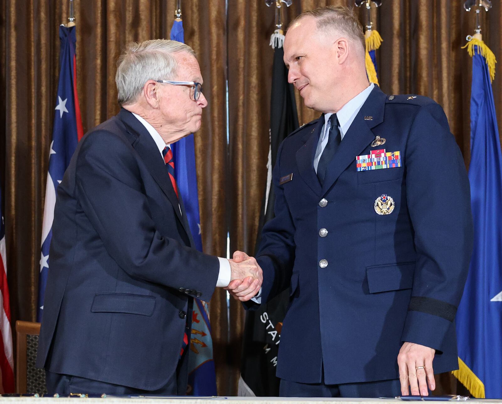 Air Force Brig Gen. Jason Bartolomei (right) shakes hands with Gov. Mike DeWine during an event on Monday at Pentagon Tower in Beavercreek. Bartolomei, along with DeWine, signed a memorandum of understanding between the State of Ohio and Air Force Research Laboratory to renew a partnership between the two entities to share science and technology information. BRYANT BILLING / STAFF