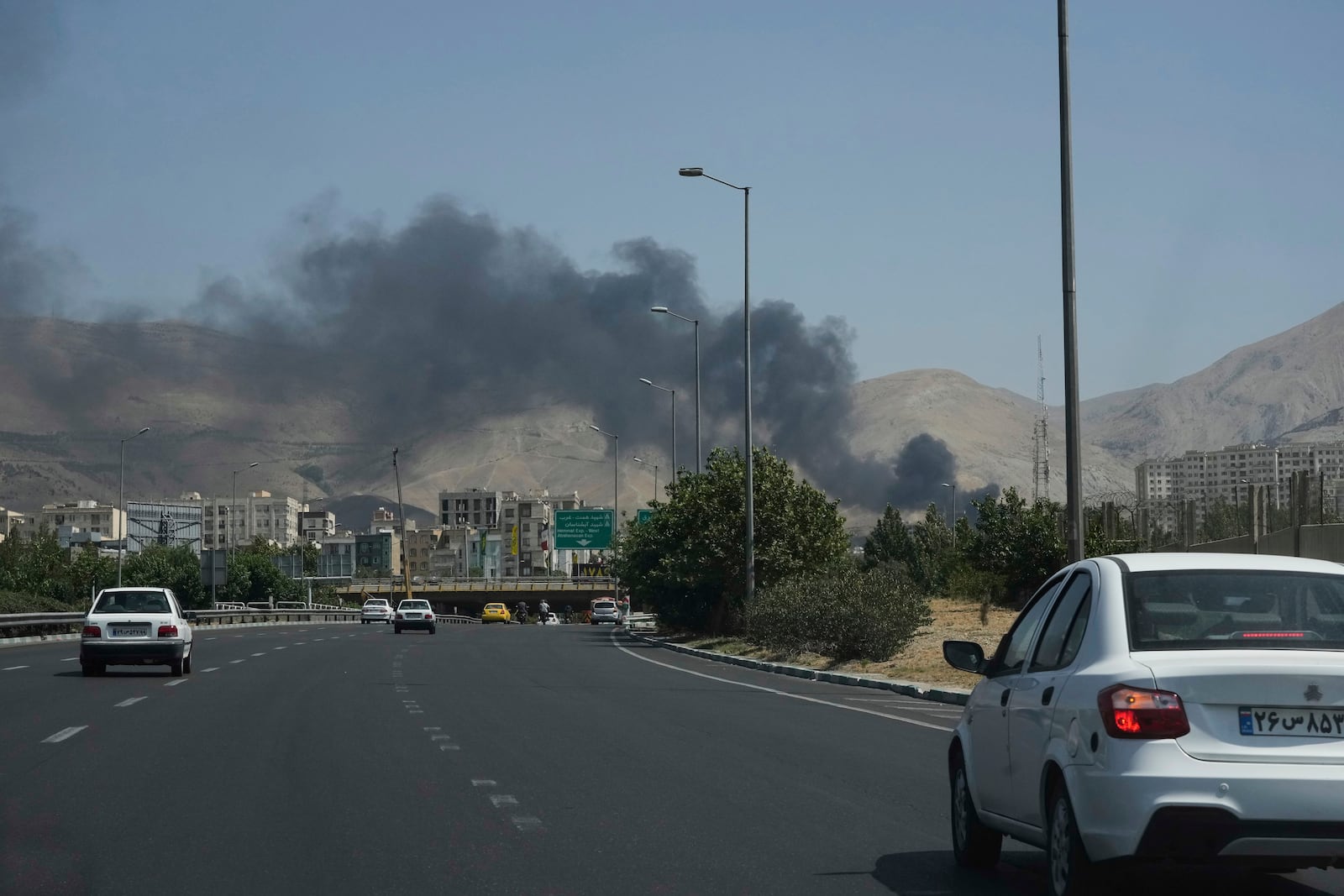 Cars drive on a highway as smoke rises from an oil storage facility after it appeared to have been struck by an Israeli strike on Saturday, in Tehran, Iran, Monday, June 16, 2025. (AP Photo/Vahid Salemi)