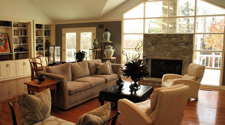 Tiered sconces direct lighting upward to set a comfortable atmosphere in the great room, which retains its original built-in bookshelves. Under a ceiling treatment with angled lines sits a stone fireplace surrounded by stacked windows.