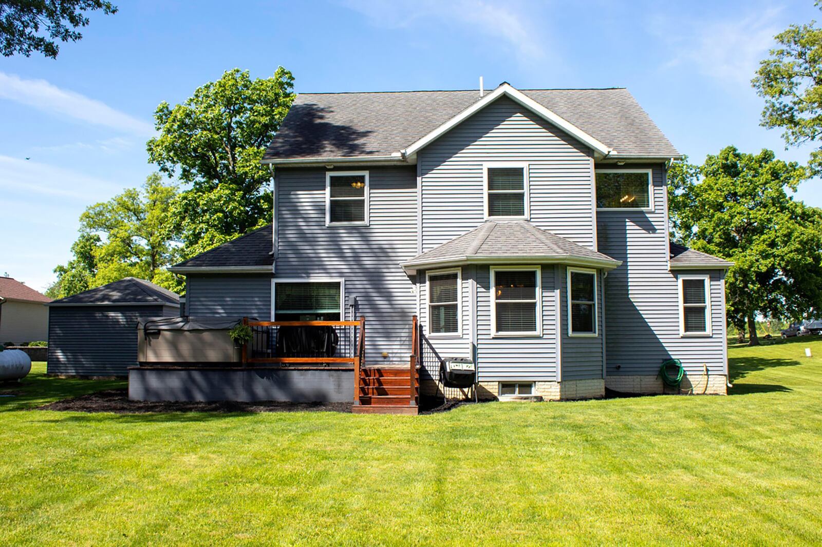 The rear of the home features a wood deck with railings and a hot tub. There is also a firepit and outbuilding.