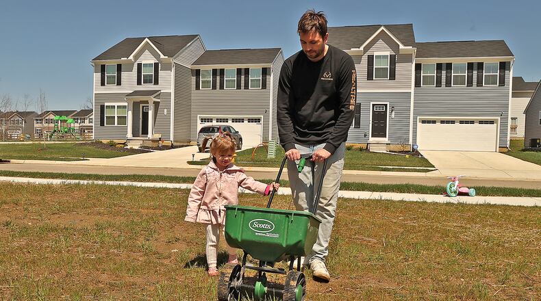 Riley Goss, 2, helps her father, Nick, sew grass seed in their new yard in the Bridgewater development Thursday. BILL LACKEY/STAFF