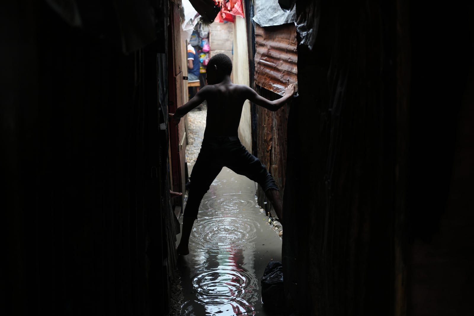A boy moves along an alleyway flooded by rain brought by Hurricane Melissa at a shelter for families displaced by gang violence in Port-au-Prince, Haiti, Wednesday, Oct. 29, 2025. (AP Photo/Odelyn Joseph)