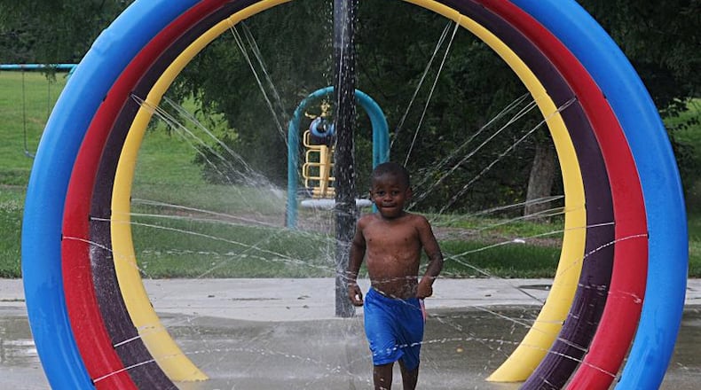 A boy beats the heat on a summer day by playing in a spray park along Germantown Street in Dayton. (Marshall Gorby/Staff)