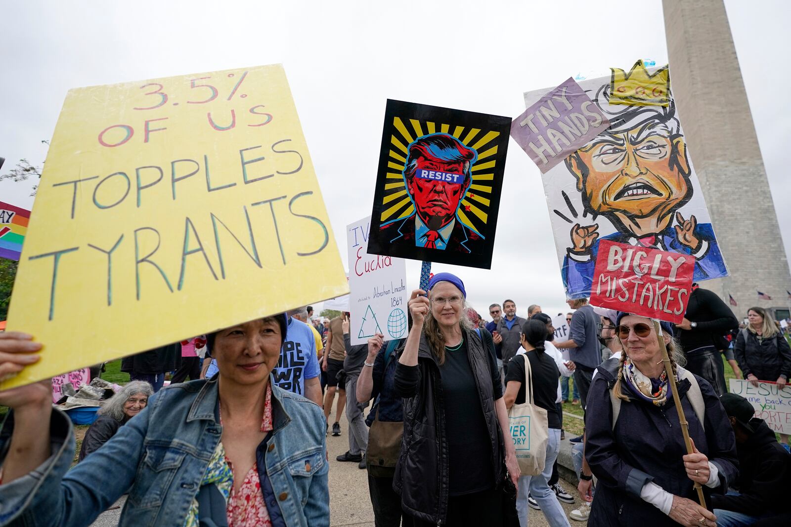 Demonstrators hold up signs during a "Hands Off!" protest against President Donald Trump at the Washington Monument in Washington, Saturday, April 5, 2025. (AP Photo/Jose Luis Magana)
