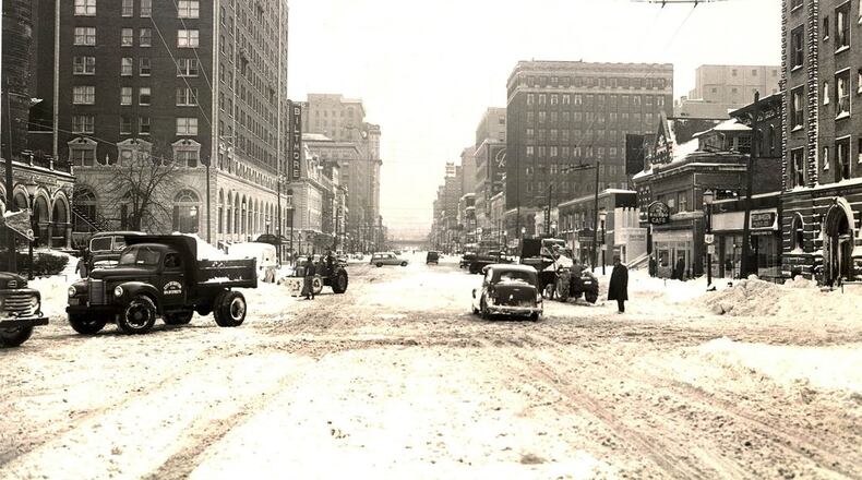 Vehicles and pedestrians attempt to navigate Main St. in downtown Dayton after nearly a foot of snow fell across the region after Thanksgiving Day in 1950. (Dayton Daily News File)