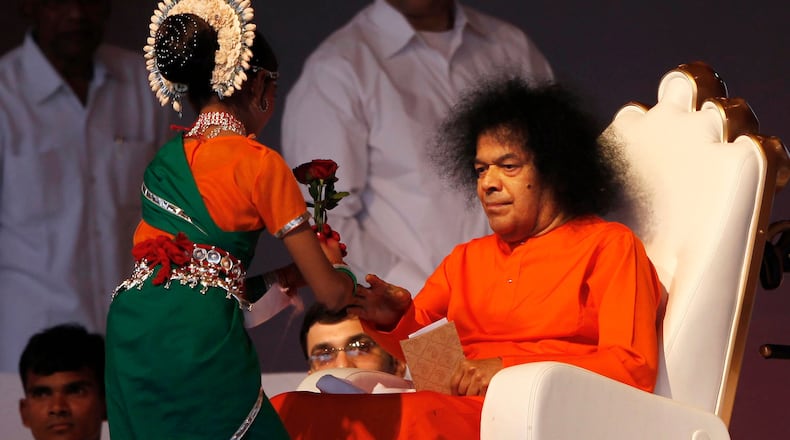 FILE - Indian spiritual leader Sathya Sai Baba, right, receives a flower from a girl at a function to meet his devotees in New Delhi, India, April 10, 2010. (AP Photo/Mustafa Quraishi, File)