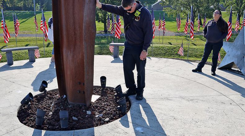 Mechanicsburg Firefighter Zach Sprinkle touches the World Trade Center artifact as he takes a moment while visiting Freedom Grove in Urbana for the 9/11 Memorial Service Monday, Sept. 11, 2023. BILL LACKEY/STAFF