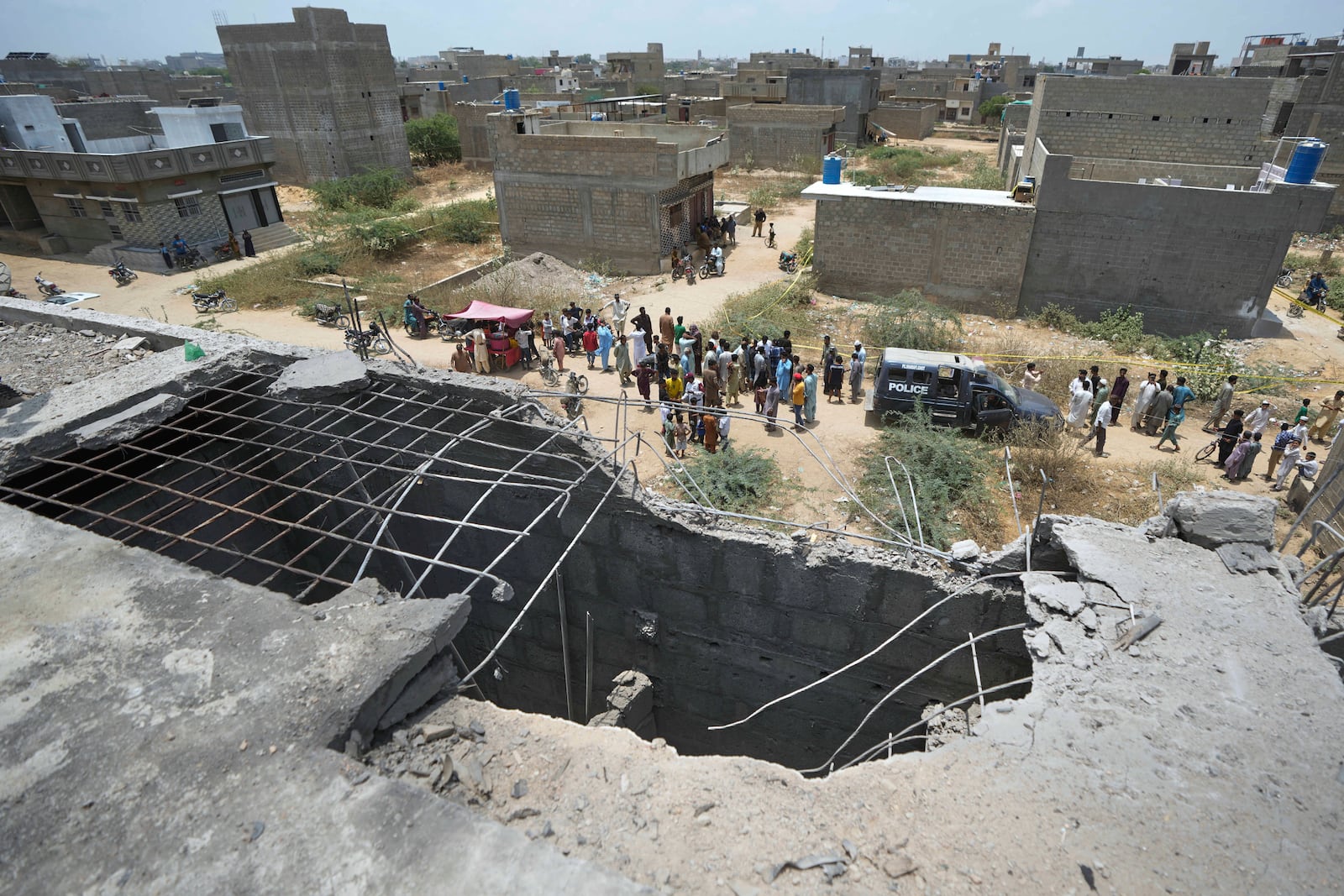 A big hole is seen on a rooftop of a house suspected to have been damaged in Indian drone attack as residents, behind, gather near a cordoned off site, where Pakistan's air defense system shot down a suspected Indian drone in Karachi, Pakistan, Thursday, May 8, 2025. (AP Photo/Fareed Khan)