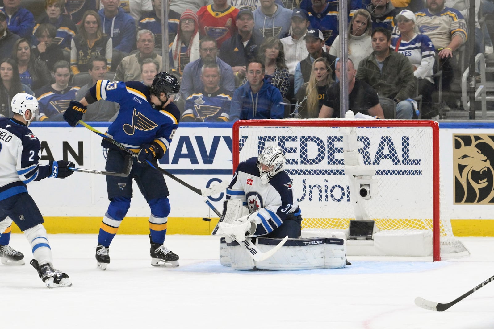 St. Louis Blues left wing Jake Neighbours (63) attempts a screen as Winnipeg Jets goaltender Connor Hellebuyck (37) makes a save during the first period in Game 6 of an NHL hockey first-round playoff series Friday, May 2, 2025, in St. Louis. (AP Photo/Jeff Le)