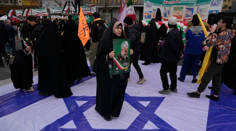 A woman holds a poster of the late commander of Iran's Revolutionary Guard expeditionary Quds Force, Gen. Qassem Soleimani, who was killed in a U.S. drone attack in 2020 in Iraq, as she stands on a banner containing an image of the Israeli flag in an annual rally marking 1979 Islamic Revolution at the Azadi, or Freedom, Street in Tehran, Iran, Wednesday, Feb. 11, 2026. (AP Photo/Vahid Salemi)