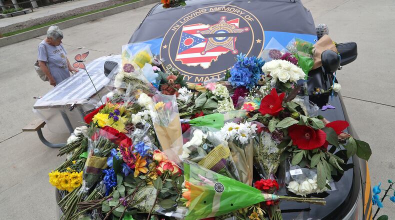 Loretta Martin looks over the messages written on a flag displayed next to a Clark County Sheriff's vehicle covered in flowers on the Springfield City Hall Plaza Tuesday, July 26, 2022. The vehicle is a memorial for Deputy Matthew Yates, who was killed Sunday on a call at Harmony Estates. BILL LACKEY/STAFF