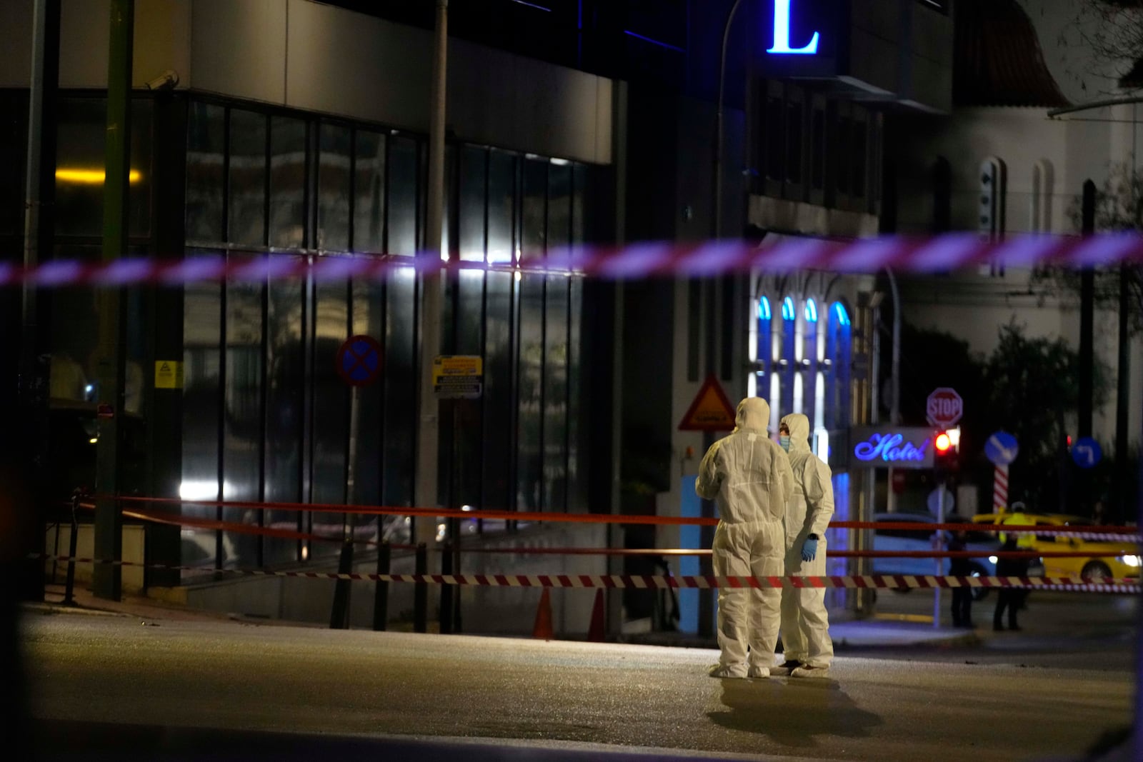 Police investigators wearing coveralls inspect the site after a bomb explosion outside of the Hellenic Train offices the company that runs Greece's railway, the building on the left, in Athens, Greece, Friday, April 11, 2025. (AP Photo/Petros Giannakouris)