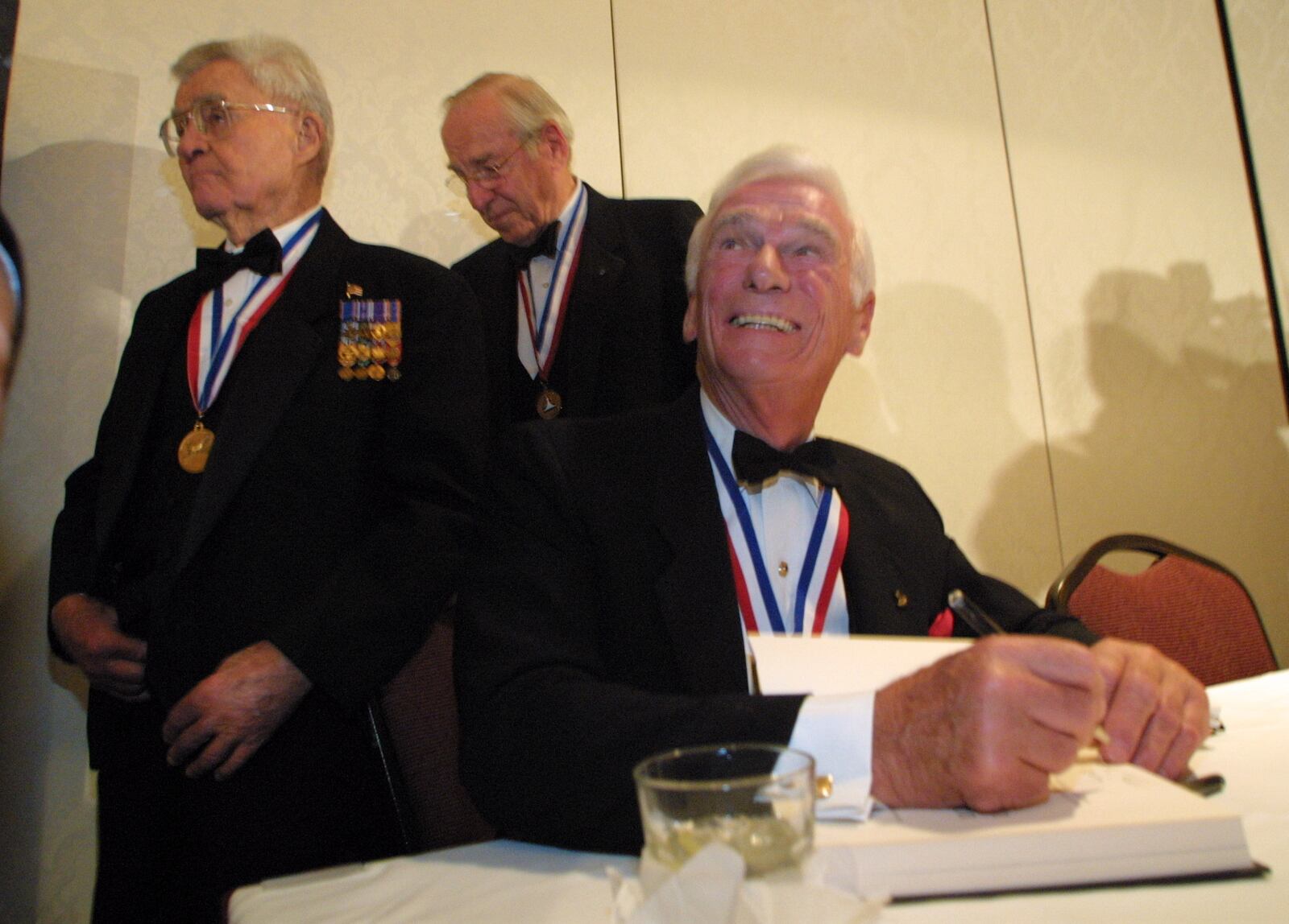 Eugene Cernan, right, last man to walk on the moon, signs an autograph Saturday during a news conference before the National Aviatioin Hall of Fame 2003 Pioneers of Flight Homecoming gala. Behind him are other enshrinees Paul Tibbets, Jr., left, who commanded the crew of the Enola Gay which dropped the first atomic bomb on and James Lovell, commander of Apollo 13.