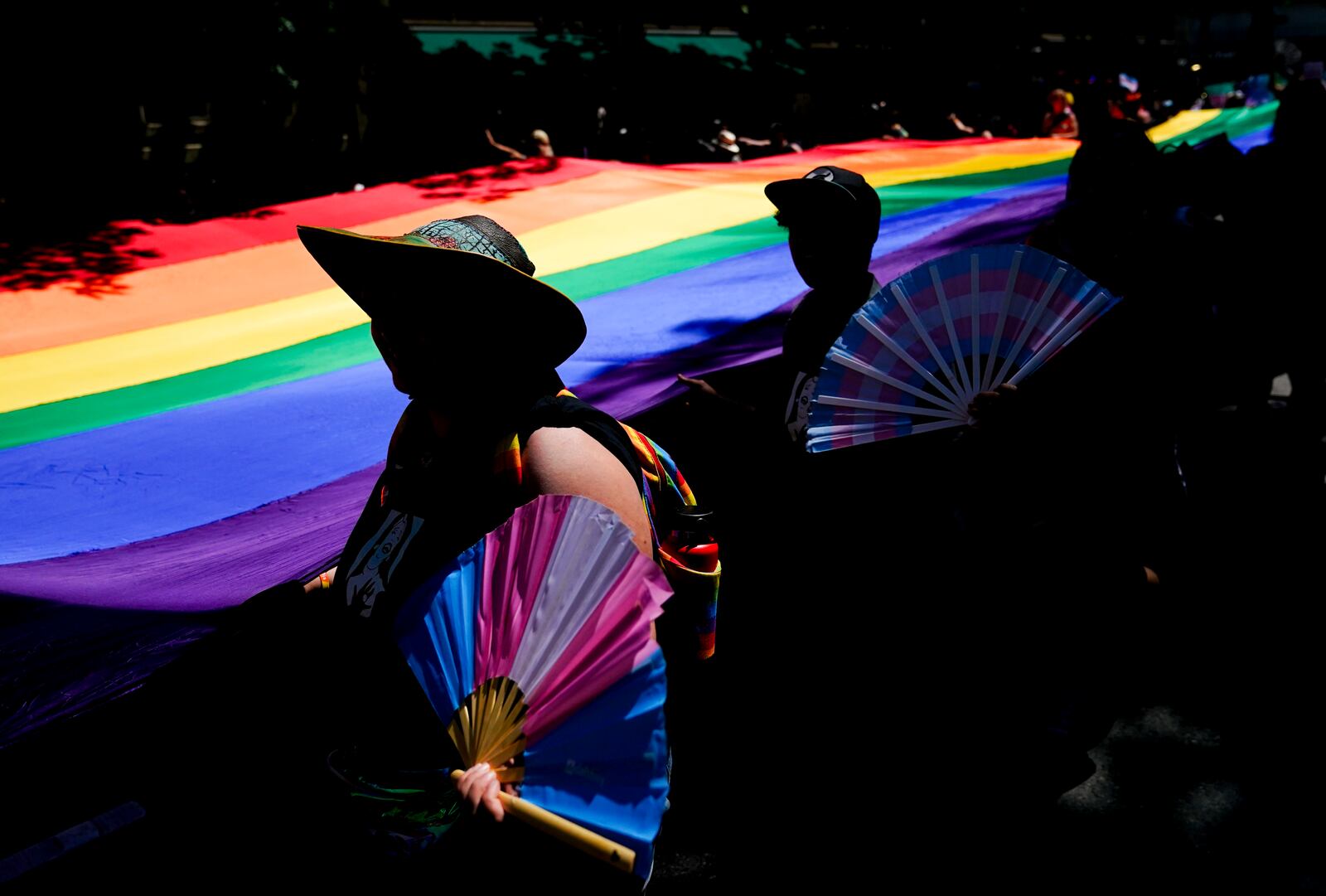 FILE - Mac Weatherill, left, and Yexara Colón Martinez, second from left, hold transgender pride fans as they help carry a large rainbow flag on their fourth anniversary during the annual Seattle Pride Parade, June 25, 2023, in Seattle. (AP Photo/Lindsey Wasson)