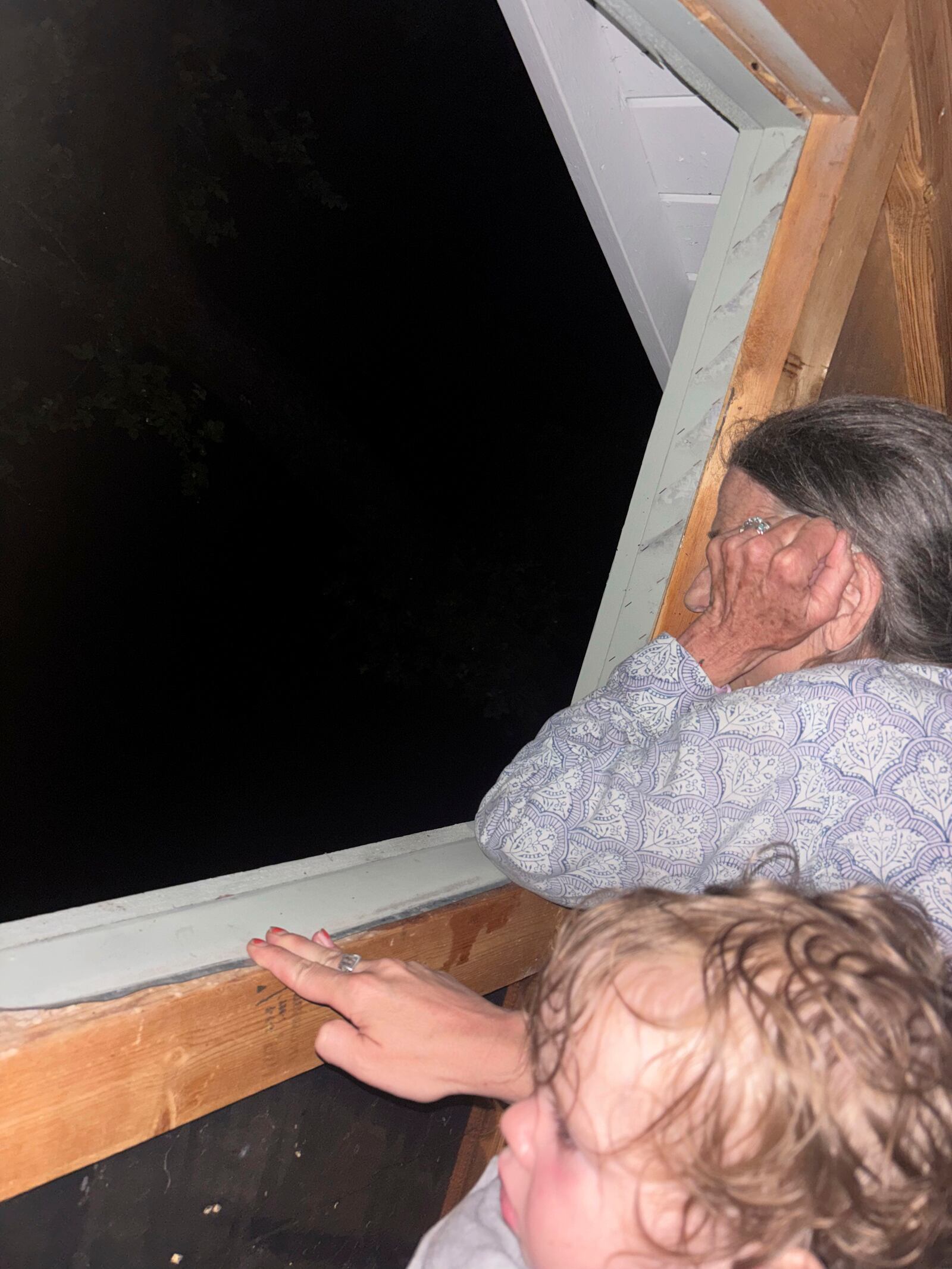 Shabd Simon-Alexander's one-year-old daughter and Jane Towler, sit in the attic of the roof of her son's cabin to escape floodwaters from the Guadalupe River in Hunt, Texas, at 6:05 a.m. on Friday, July 4, 2025. (Shabd Simon-Alexander via AP)