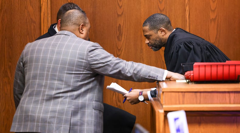 A judge conferences with attorney Ryan Nelson (front left) and Montgomery County assistant prosecutor Bryan Moore (back left) during a hearing in Montgomery County Common Pleas Court on Wednesday, Jan. 28. Matthew Currie, an Oakwood attorney accused of stalking and secretly recording a teenage girl and other women, was not in attendance. Currie, who has a rare parkinsonism disease, is receiving care in an ICU, according to Nelson. BRYANT BILLING/STAFF