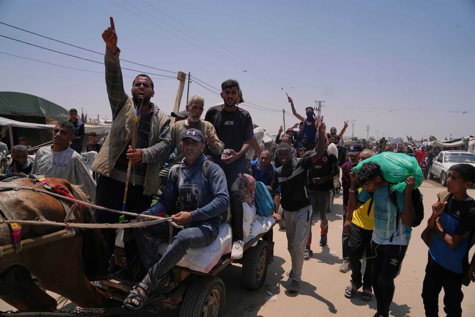Palestinians wave to the camera while carrying bags containing food and humanitarian aid packages delivered by the Gaza Humanitarian Foundation, a U.S.-backed organization, in Rafah, southern Gaza Strip, Tuesday, June 10, 2025. (AP Photo/Abdel Kareem Hana)