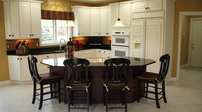 Granite tops the semi-circular island/breakfast bar at the entrance to the open kitchen. Oversized white cabinets with raised-panel doors surround the work space.