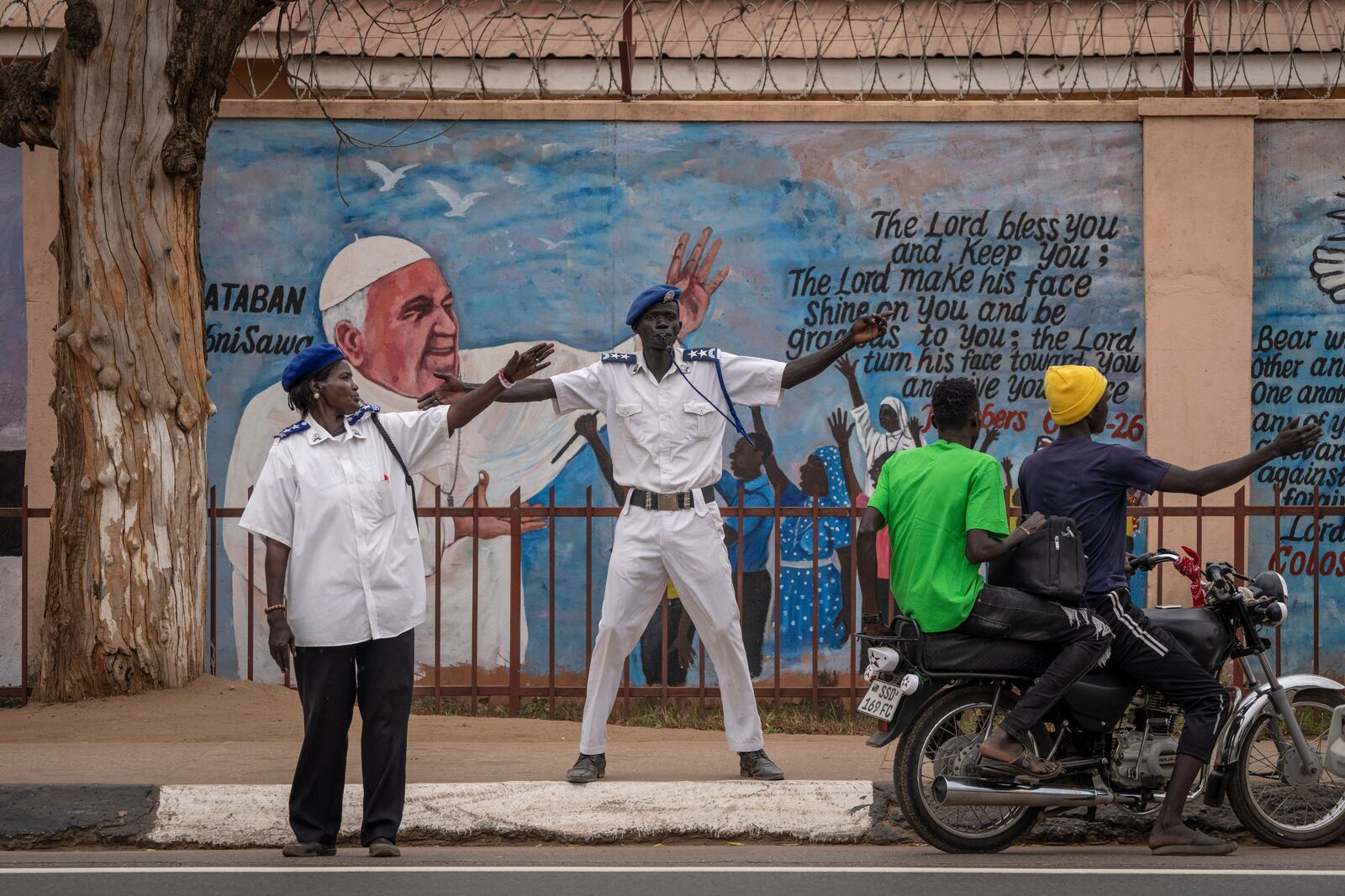 FILE - Standing by a mural of Pope Francis on a church, traffic police direct vehicles to get off the road as a government vehicle convoy passes through Juba, South Sudan, Feb. 2, 2023. (AP Photo/Ben Curtis, File)