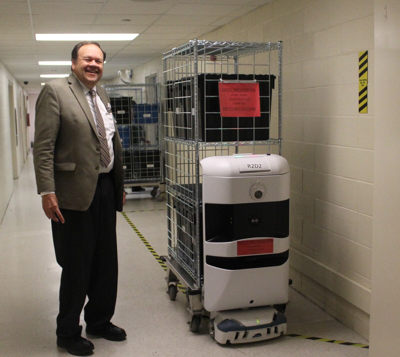 David Starkey, Kettering  Health Networks's director of  materials management and biomedical engineering, stands with a TUG nicknamed R2D2.  The robots were introduced to Kettering Hospital in January.