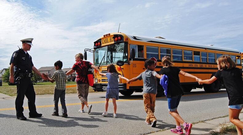 A West Chester Twp. police officer gives high-fives to Endeavor Elementary students as they board a bus to be transported to Lakota West Freshman School after a bomb threat forced the school to be evacuated in 2015. ERIC SCHWARTZBERG/STAFF