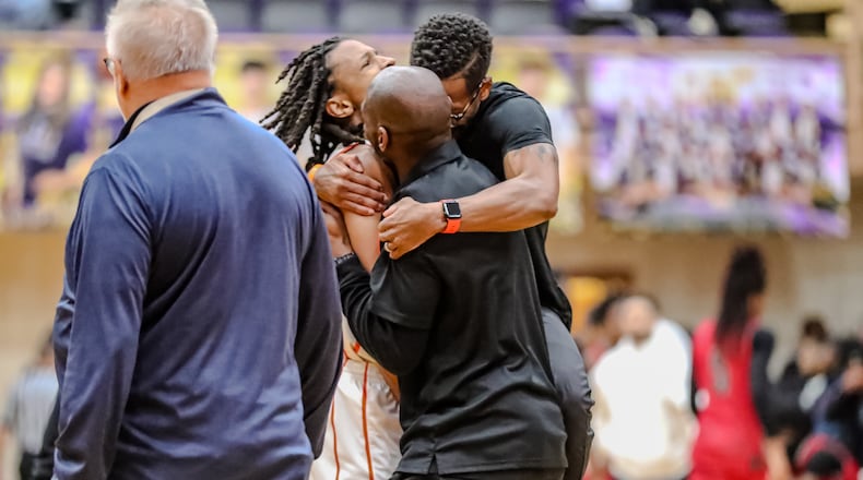 Beavercreek High School coach Isaiah Williams (right) hugs his son, Isaiah-Michael Williams (left) and assistant coach Malcolm Fields (front) after beating Princeton 49-43 in a Division I district final game on Saturday, March 1 at the Vandalia Butler Student Activities Center. MICHAEL COOPER/STAFF