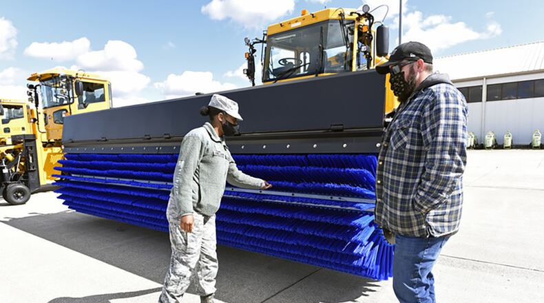 Senior Airman Royality Jones-Gavin, command support, 88th Air Base Wing, inspects an Oshkosh airfield snow broom with heavy equipment operator Dustin McIver, 88th Air Base Wing Civil Engineer Group, before test driving the big machine at Wright-Patterson Air Force Base Oct. 2. CEG drivers paraded the snow removal equipment across the airfield for review by 88th Air Base Wing and installation Commander Col. Patrick Miller to demonstrate the equipment needed to keep the base and the airfield operational. U.S. AIR FORCE PHOTO/TY GREENLEES