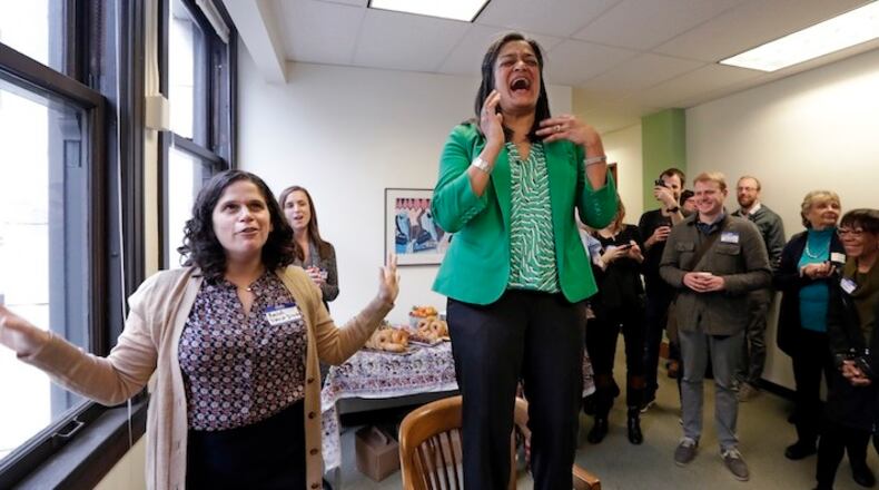 Rep. Pramila Jayapal, D-Seattle, center, stands atop a chair while addressing supporters and reacts to a comment from her district director, Rachel Berkson, left, while marking the official opening of her Seattle district office, Tuesday, Jan. 17, 2017. Jayapal is one of more than 50 House Democrats who will not attend the swearing-in ceremony for President-elect Donald Trump on Friday. She said that she will instead attend to constituent business in Seattle, before flying to D.C. Friday evening to march in the Women's March on Washington on Saturday. (AP Photo/Elaine Thompson)