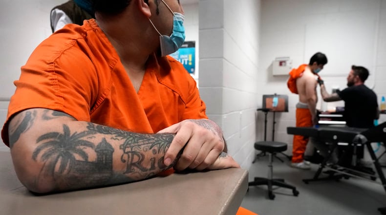 Gilberto watches and waits his turn, as Jamie prepares to have a bullet scar hidden with a tattoo at the DuPage County Jail, Thursday, Feb. 3, 2022, in Wheaton, Ill. To get the jail's backing in their job hunts, participants must graduate. And to graduate, they must have their gang tattoos removed or covered with non-gang tattoos. It's proof they're serious about forsaking their old lives and aren't merely pining for leniency from their jailers or judges, said DuPage County Sheriff James Mendrick. (AP Photo/Charles Rex Arbogast)