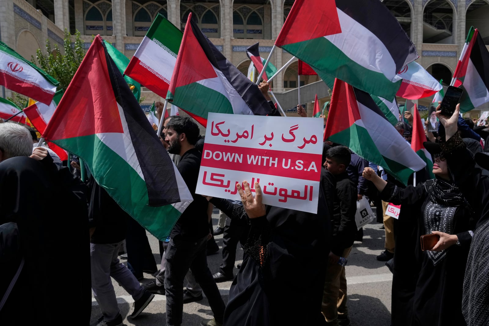 An Iranian worshipper holds up a placard as the others wave Iranian and Palestinian flags during an anti-Israeli and anti-U.S. protest after their Friday prayers in Tehran, Iran, Friday, July 25, 2025. (AP Photo/Vahid Salemi)