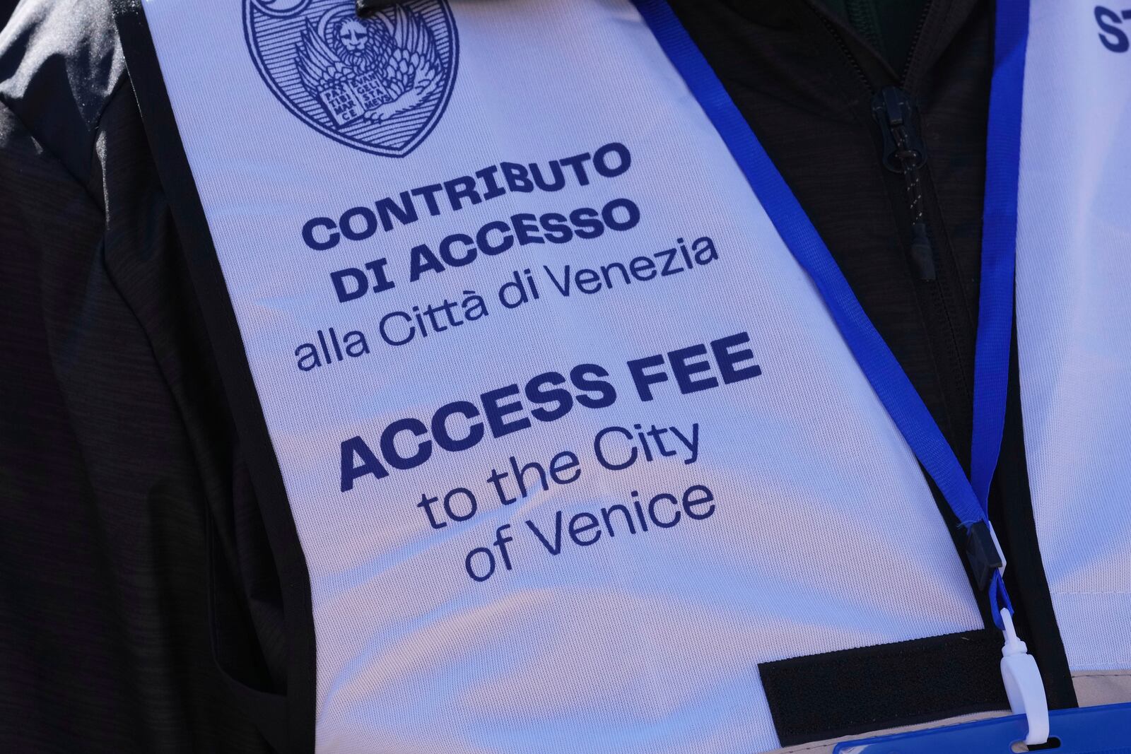 A steward's gilet states an arrival tax fee for tourists visiting Venice, Italy, Friday, April 18, 2025. (AP Photo/Antonio Calanni)