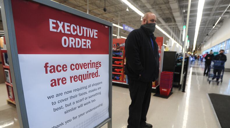 Meijer meat team leader, Tyler Winthrop, stands next to one of the executive order signs at the entrance to the Meijer store on Wilmington Pike Monday. Winthrop said, that all customers have been very compliant to the order.  MARSHALL GORBY\STAFF