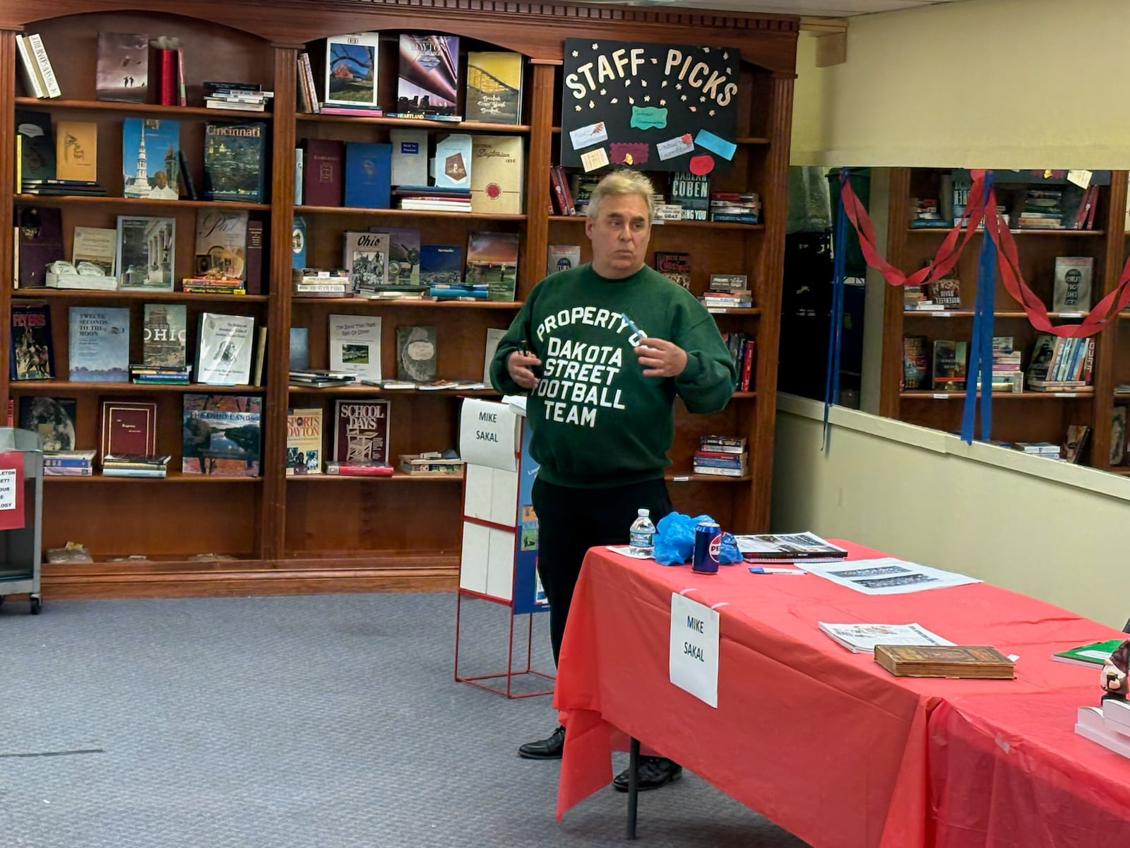 Mike Sakal, wearing his Dakota Street Football sweatshirt, talks to the crowd at his book signing last Saturday at the New & Olde Pages Bookshop in Englewood. TOM ARCHDEACON / CONTRIBUTED PHOTO