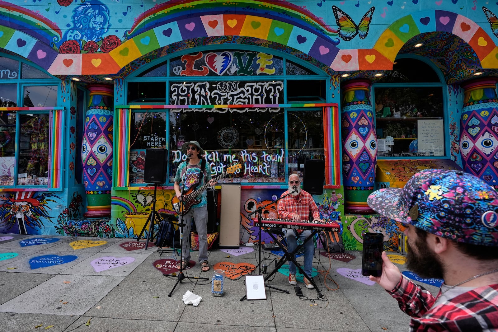 A man uses a cellphone to record musicians performing during Haight Street Daydream, a community event celebrating the 60th anniversary of the Grateful Dead, in San Francisco, Saturday, July 19, 2025. (AP Photo/Godofredo A. Vasquez)