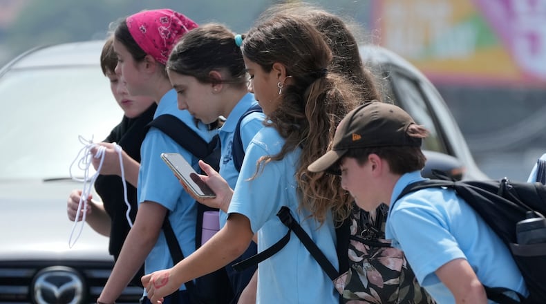 A school girl uses her phone as she walks with a group of kids in Sydney, Monday, Dec. 8, 2025. (AP Photo/Rick Rycroft)