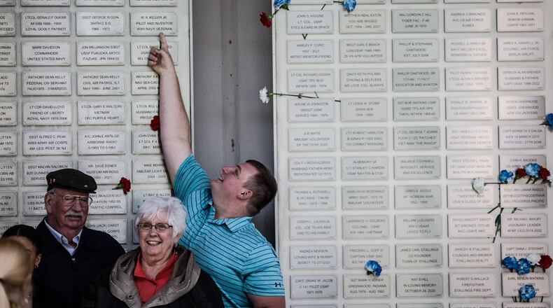 Ash Williams from New Madison points up at his Great Grandfathers, WWII veteran Robert Schlotterbeck's plack.  
The Air Force Museum held its first Honor Plate Ceremony since the pandemic three years ago. A total of 475 new names were added to the wall. After the ceremony, family and friends hung flowers near their loved one's plates. JIM NOELKER/STAFF