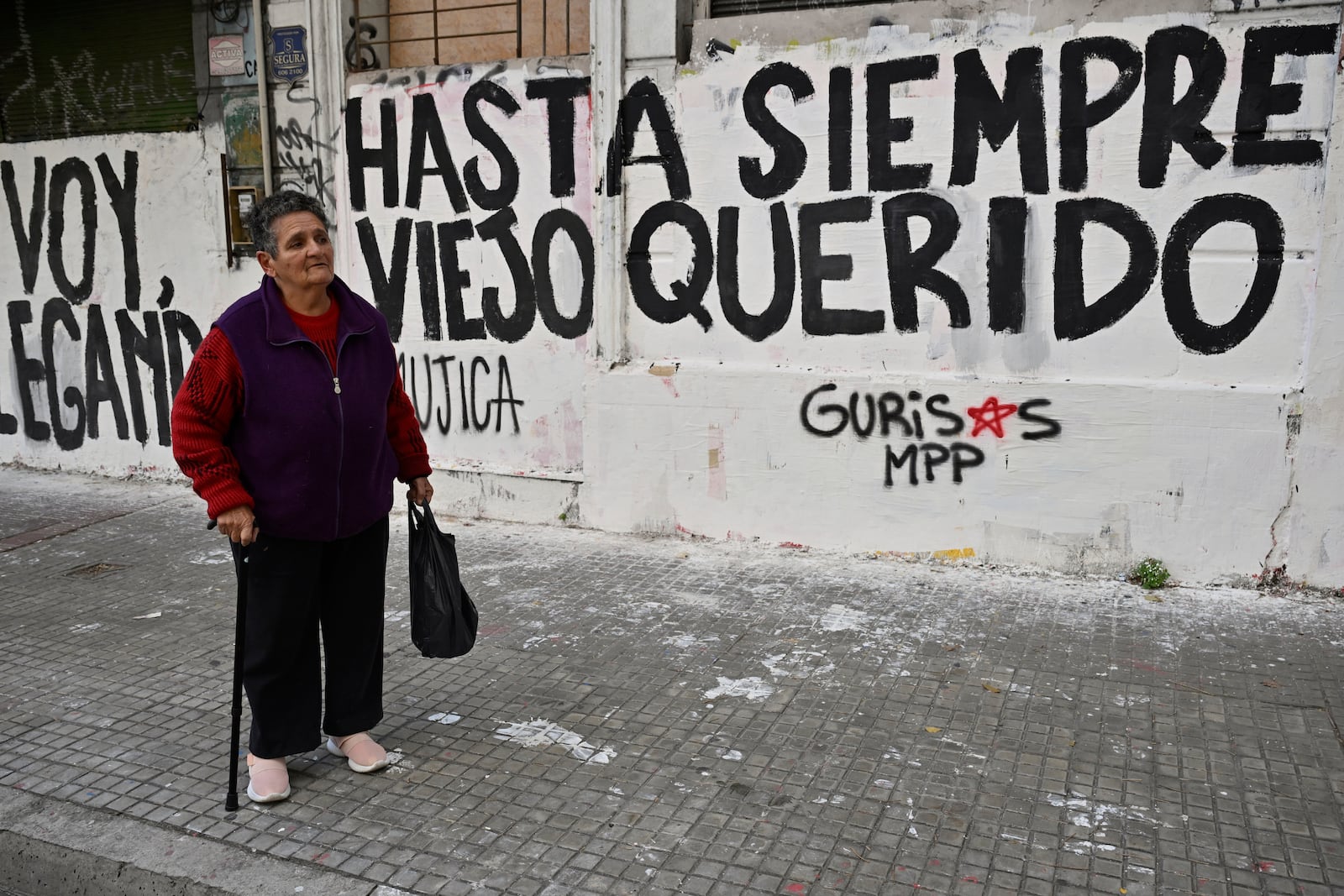 A woman watches the funeral procession of former President Jose Mujica from the presidential palace to the National Assembly, next to graffiti that reads in Spanish: "Farewell dear old man," in Montevideo, Uruguay, Wednesday, May 14, 2025. (AP Photo/Santiago Mazzarovich)