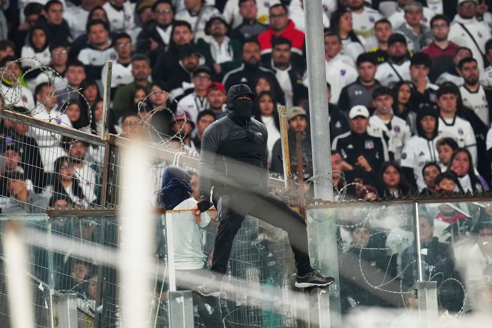 A fan climbs on a glass panel in the stands during a Copa Libertadores Group E soccer match between Chile's Colo Colo and Brazil's Fortaleza at Monumental Stadium in Santiago, Chile, Thursday, April 10, 2025. (AP Photo/Esteban Felix)
