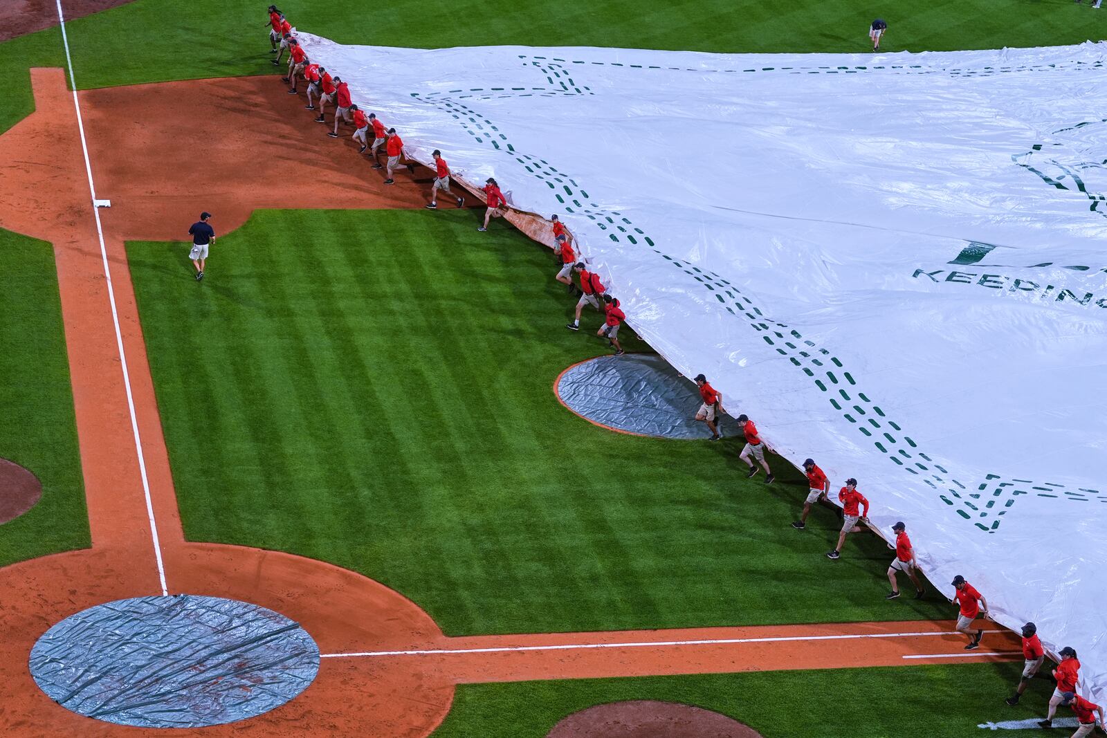 The grounds crew covers the field with a tarp during a rain delay in the fourth inning of a baseball game between the Boston Red Sox and Cincinnati Reds at Fenway Park, Tuesday, July 1, 2025, in Boston. (AP Photo/Charles Krupa)